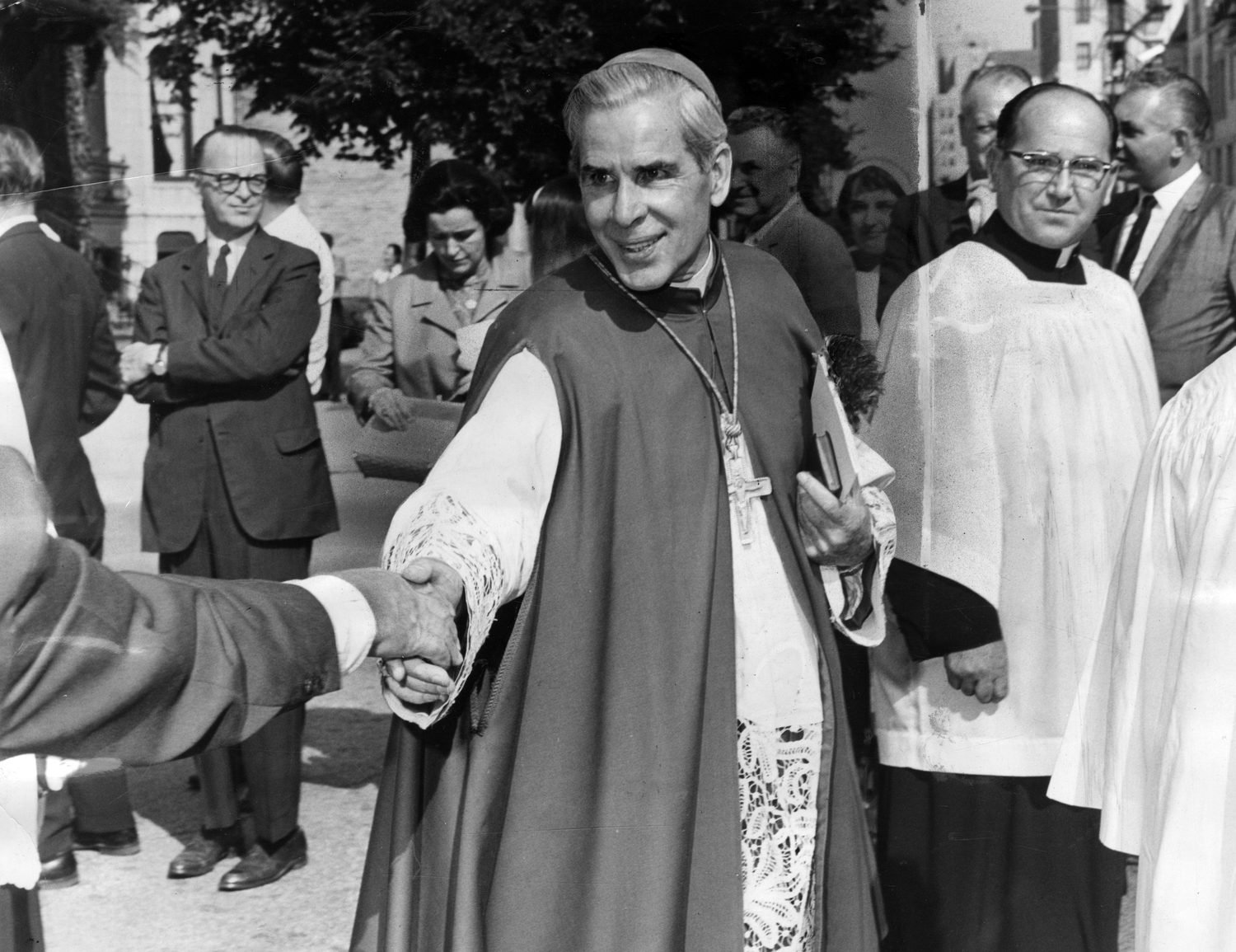 Archbishop Sheen shaking hands with a man in a crowd
