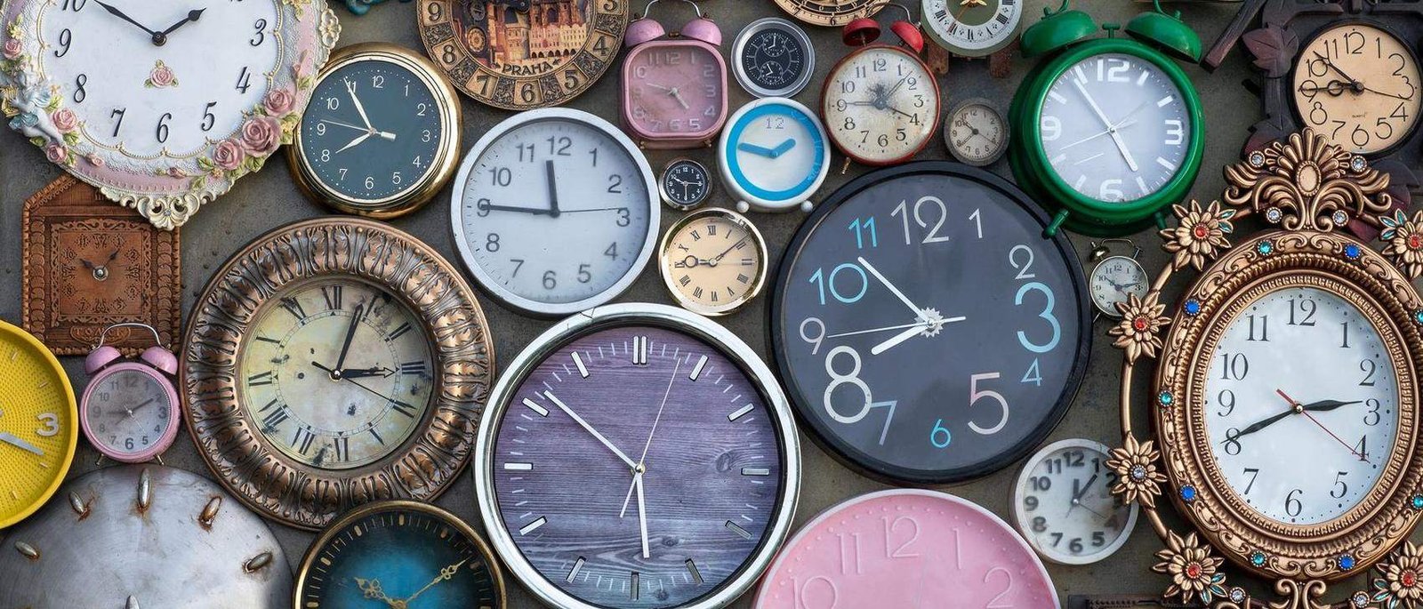 A wall of vintage clocks, each showing a different hour