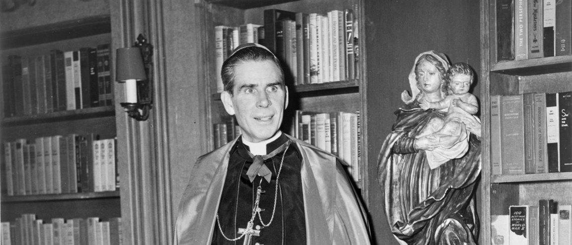 Bishop Sheen standing among the shelves of his library
