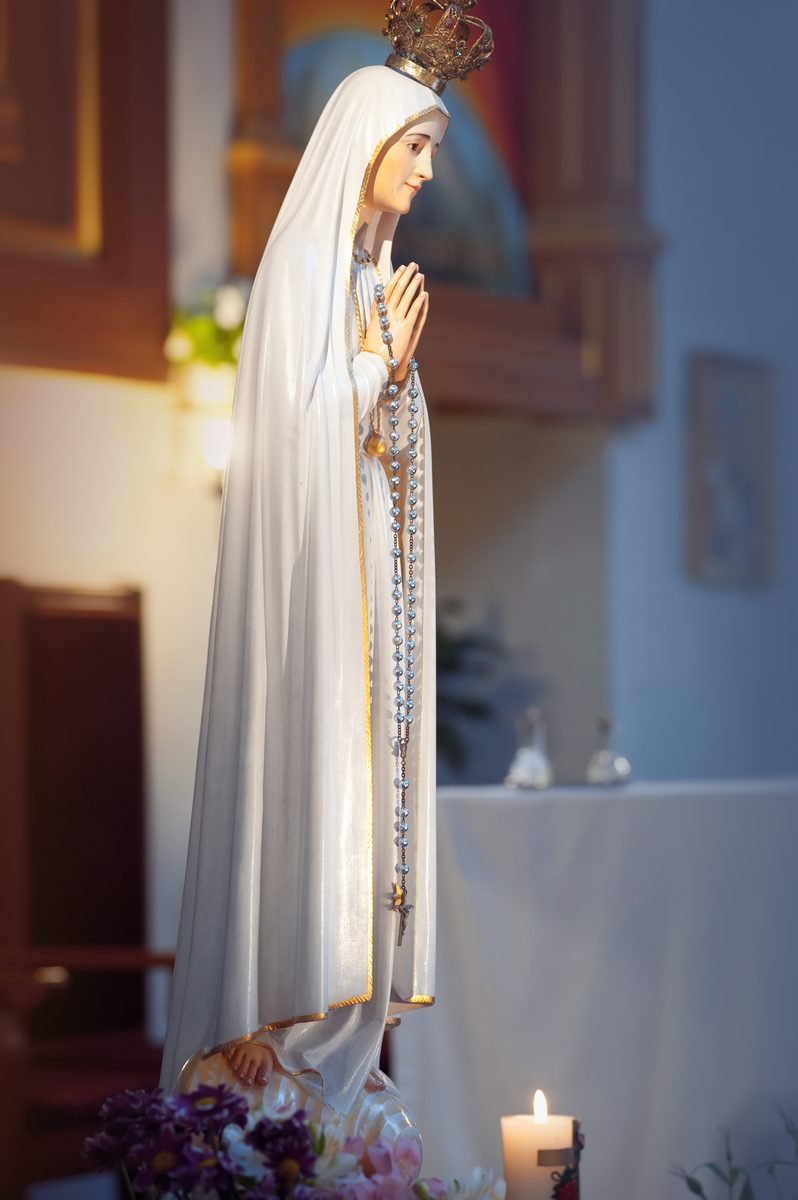 A statue of Our Lady holding a rosary, before a lit candle